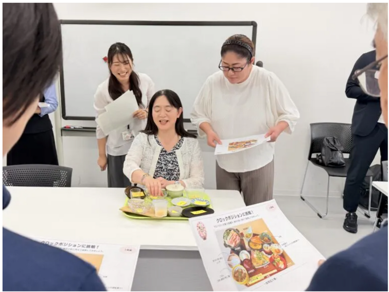 テーブル上の食器の配置を説明する講師と熱心に聞き入る受講生